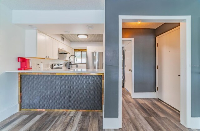 kitchen featuring stainless steel fridge, white cabinetry, stove, wood-type flooring, and sink