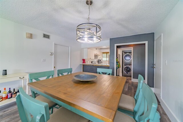 dining area featuring dark hardwood / wood-style floors, a textured ceiling, a notable chandelier, and stacked washer / dryer