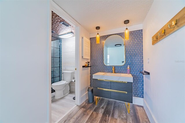 bathroom featuring toilet, hardwood / wood-style floors, vanity, a textured ceiling, and tile walls