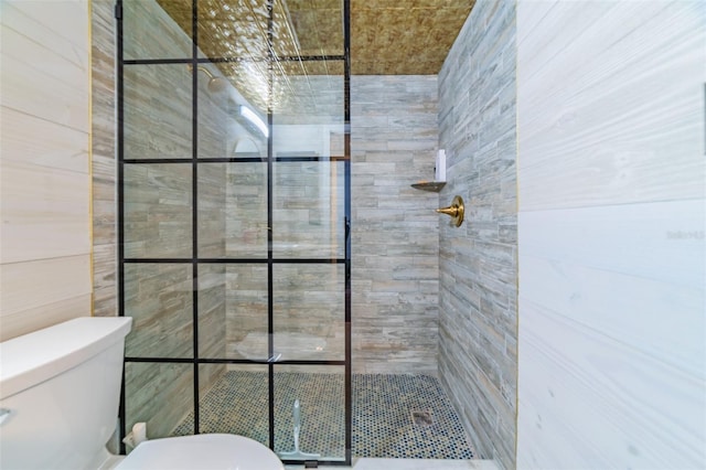 bathroom with tiled shower, toilet, and tile walls