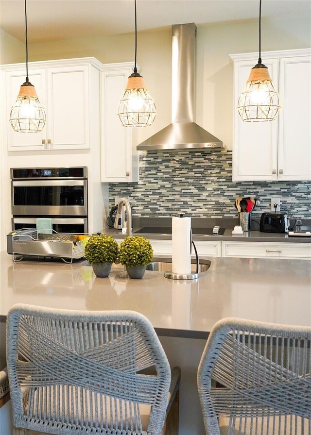 kitchen with tasteful backsplash, white cabinets, wall chimney exhaust hood, a breakfast bar area, and double oven