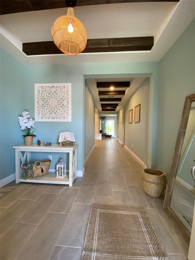 corridor featuring tile patterned floors, beam ceiling, and a raised ceiling