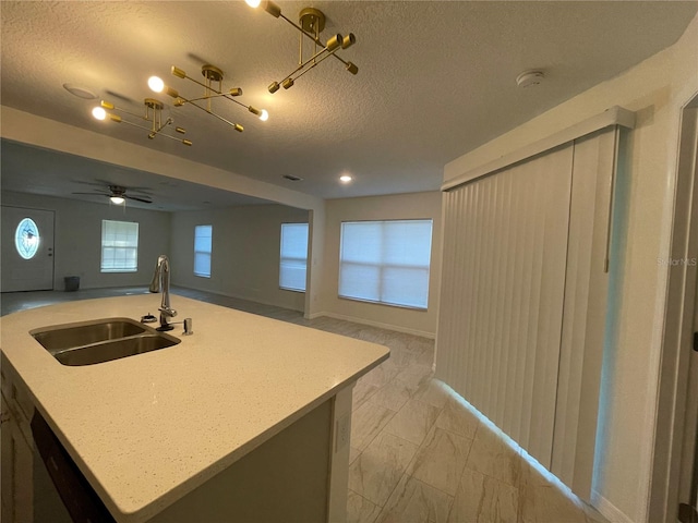 kitchen featuring a textured ceiling, a healthy amount of sunlight, an island with sink, and sink