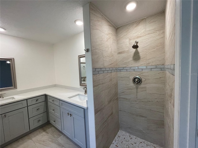 bathroom featuring vanity, a textured ceiling, a tile shower, and tile patterned floors