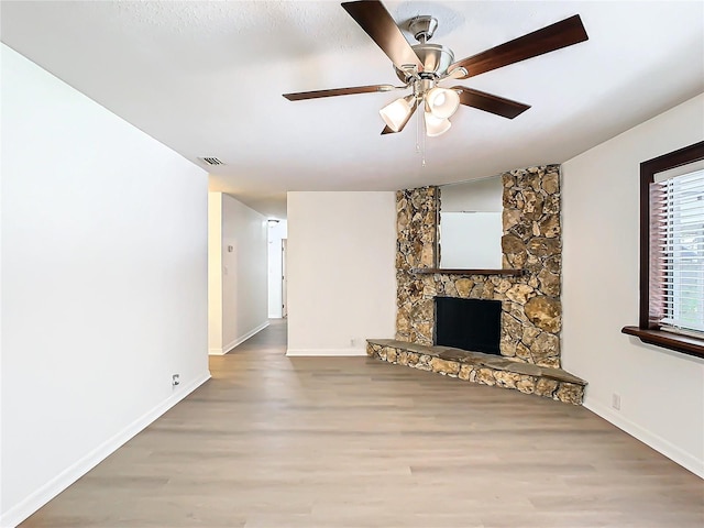 unfurnished living room featuring a stone fireplace, ceiling fan, and wood-type flooring