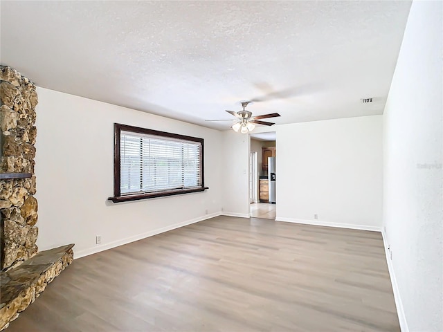 unfurnished living room with hardwood / wood-style floors, ceiling fan, a stone fireplace, and a textured ceiling