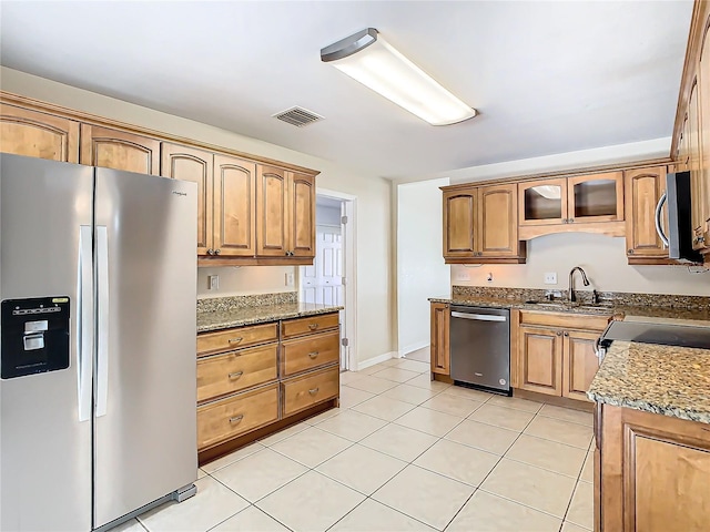 kitchen with stone countertops, sink, light tile patterned floors, and stainless steel appliances