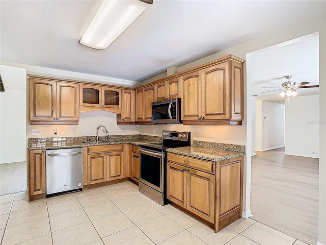 kitchen with ceiling fan, sink, dark stone counters, light tile patterned floors, and appliances with stainless steel finishes