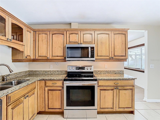 kitchen with stone counters, sink, light tile patterned floors, and stainless steel appliances