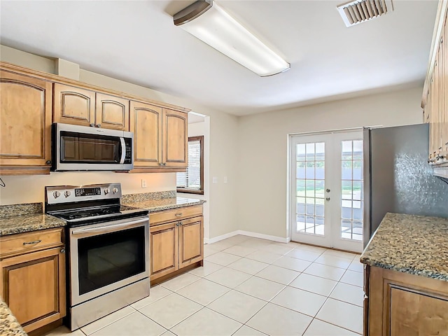 kitchen with dark stone countertops, light tile patterned floors, stainless steel appliances, and french doors