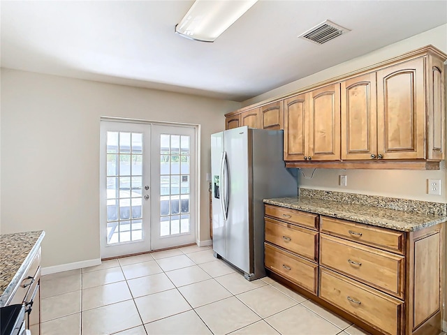 kitchen with light tile patterned flooring, light stone counters, stainless steel fridge with ice dispenser, and french doors