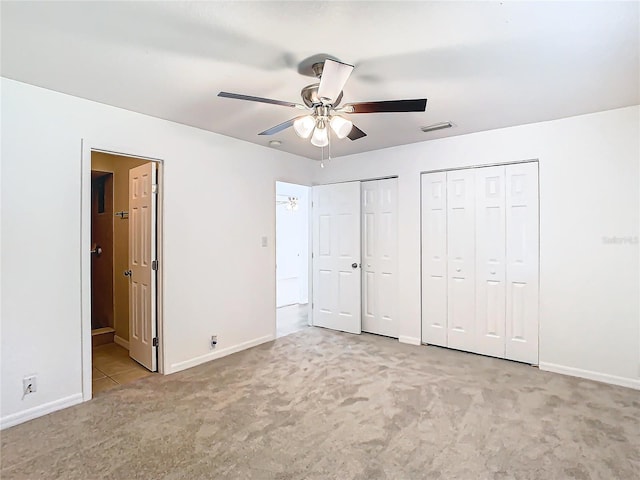 unfurnished bedroom with ceiling fan, light carpet, and multiple closets