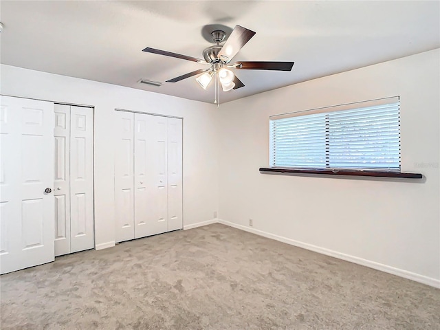 unfurnished bedroom featuring multiple closets, ceiling fan, and light carpet