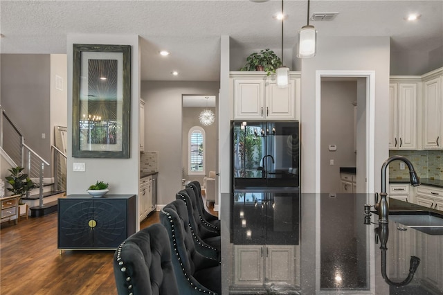 kitchen with dark wood-type flooring, a sink, white cabinetry, visible vents, and tasteful backsplash