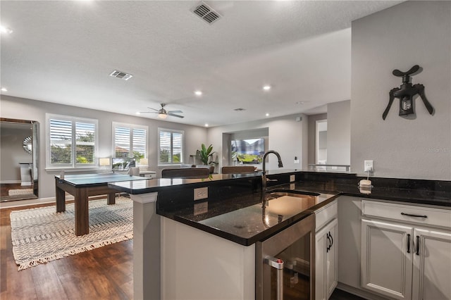 kitchen with dark wood finished floors, visible vents, a sink, dark stone counters, and beverage cooler