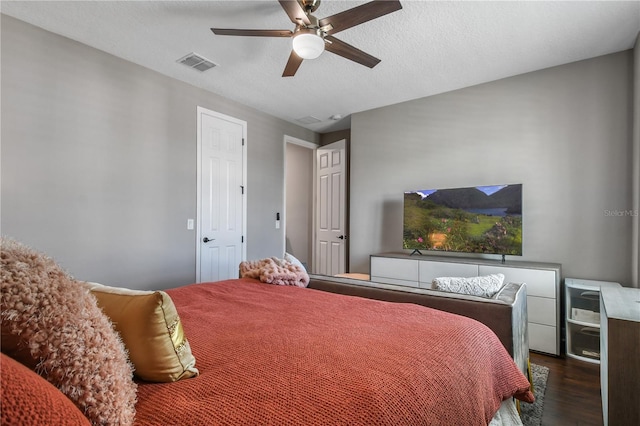 bedroom with a ceiling fan, visible vents, a textured ceiling, and wood finished floors