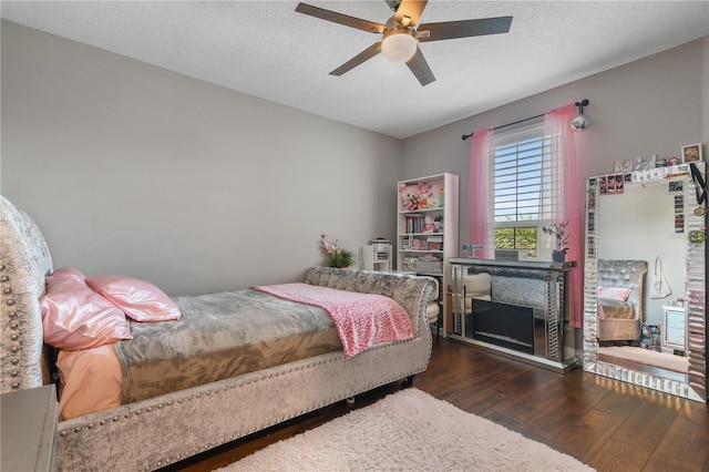 bedroom with a ceiling fan, a fireplace, a textured ceiling, and wood finished floors