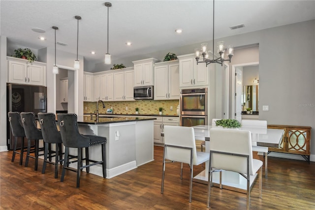 kitchen featuring a center island with sink, visible vents, dark countertops, appliances with stainless steel finishes, and a sink