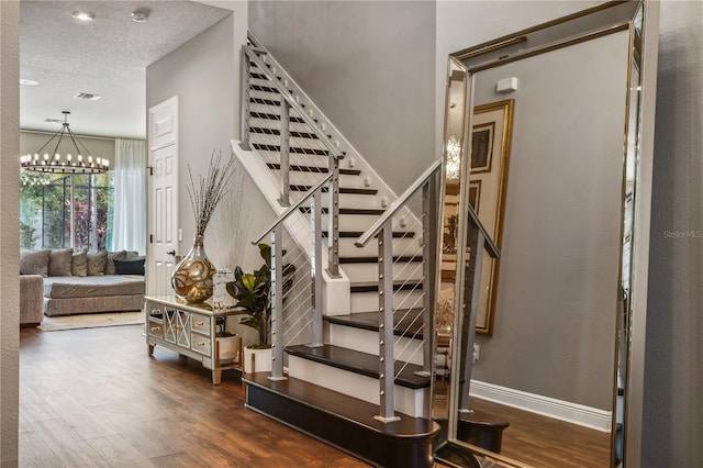 stairway featuring a chandelier, a textured ceiling, wood finished floors, visible vents, and baseboards