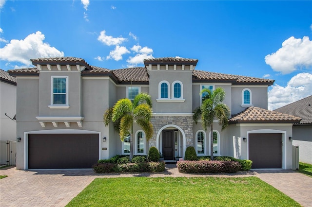 mediterranean / spanish house with stone siding, a front yard, decorative driveway, and stucco siding