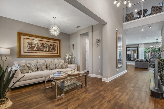 living area with dark wood-type flooring, a towering ceiling, baseboards, visible vents, and an inviting chandelier