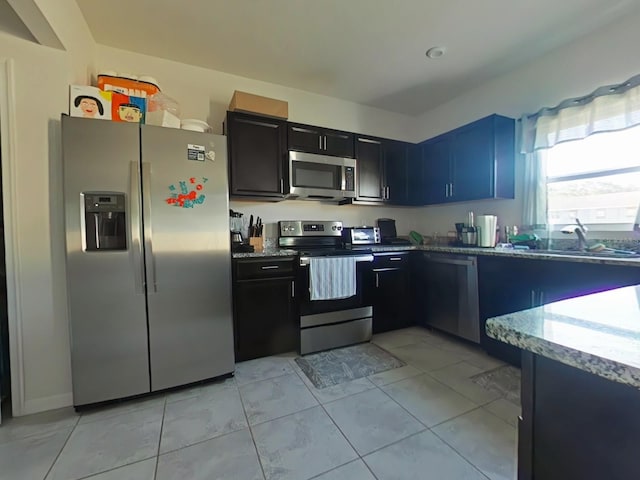 kitchen with light tile patterned flooring, light stone countertops, appliances with stainless steel finishes, and sink