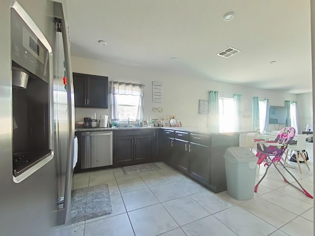 kitchen featuring kitchen peninsula, appliances with stainless steel finishes, light tile patterned floors, and plenty of natural light