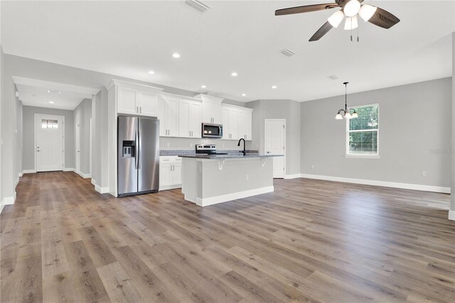 kitchen featuring white cabinetry, stainless steel appliances, hardwood / wood-style floors, a kitchen breakfast bar, and a center island with sink