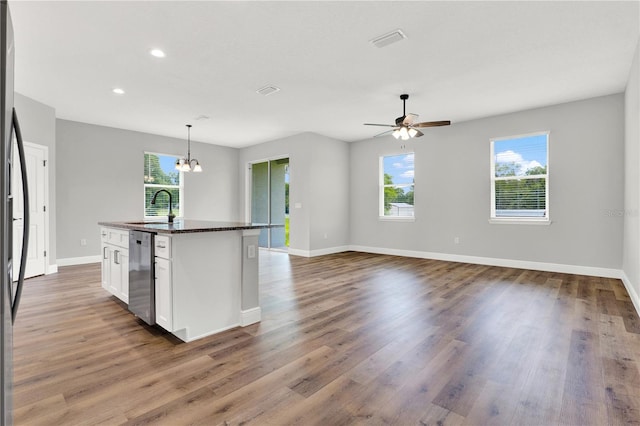 kitchen featuring white cabinets, a center island with sink, ceiling fan with notable chandelier, dishwasher, and hardwood / wood-style flooring