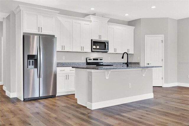 kitchen featuring appliances with stainless steel finishes, white cabinetry, hardwood / wood-style flooring, and a kitchen island with sink