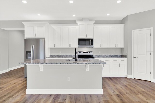 kitchen featuring stone counters, light hardwood / wood-style flooring, appliances with stainless steel finishes, and an island with sink