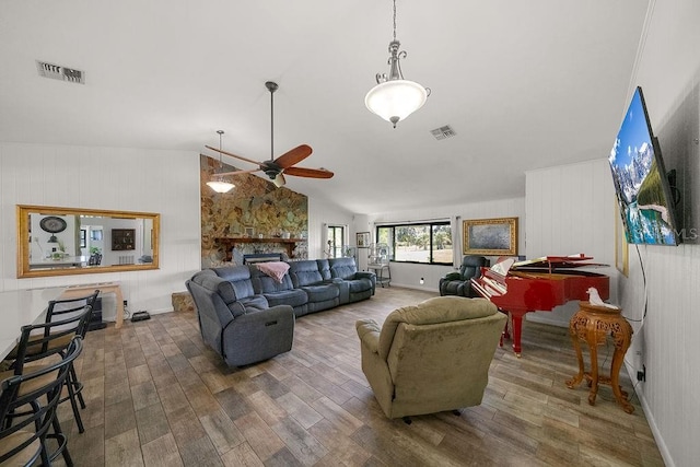 living room with lofted ceiling, hardwood / wood-style flooring, ceiling fan, and a stone fireplace