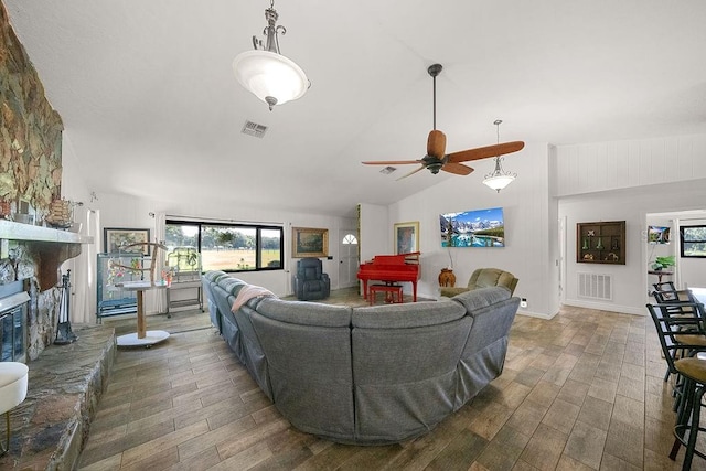 living room with ceiling fan, a stone fireplace, and vaulted ceiling