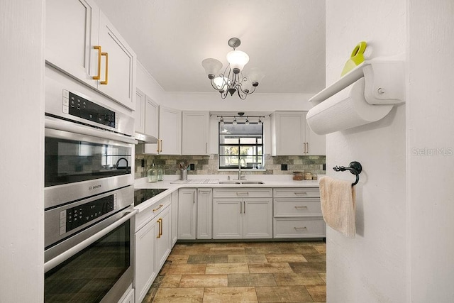 kitchen featuring a chandelier, stainless steel double oven, black electric cooktop, sink, and backsplash