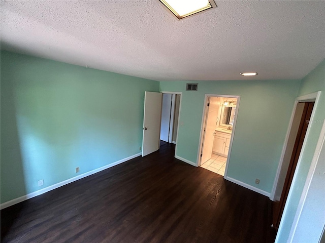 unfurnished bedroom featuring a textured ceiling, dark hardwood / wood-style flooring, and connected bathroom