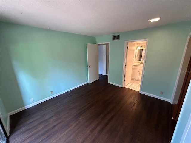 unfurnished bedroom featuring a textured ceiling, dark wood-type flooring, and ensuite bathroom