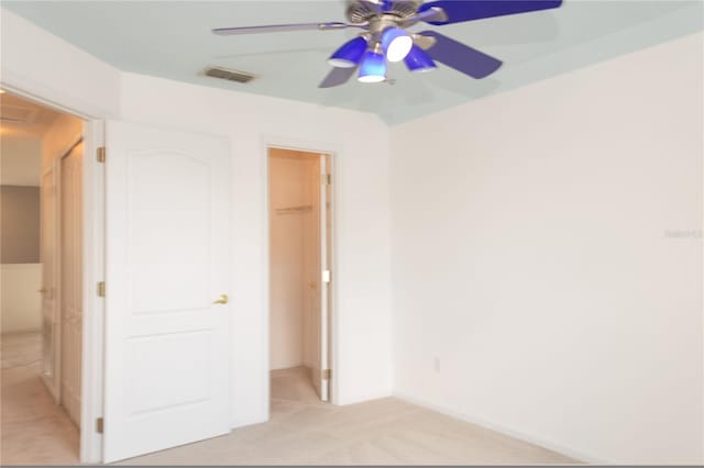 unfurnished bedroom with a walk in closet, ceiling fan, a closet, and light carpet