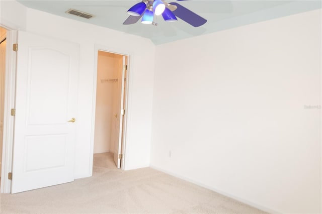 unfurnished bedroom featuring a walk in closet, a closet, ceiling fan, and light colored carpet