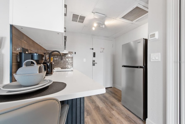 kitchen featuring light wood-style flooring, white cabinets, visible vents, and freestanding refrigerator