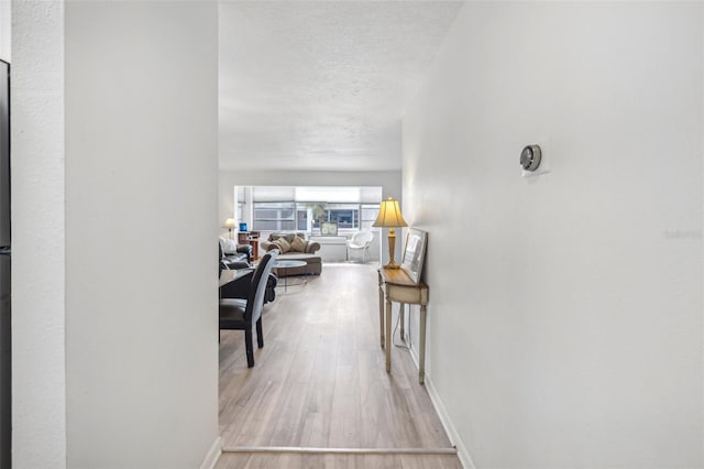 corridor with a textured ceiling and light hardwood / wood-style flooring