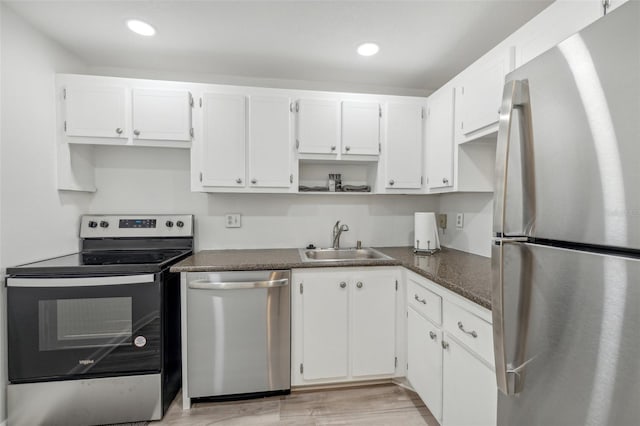 kitchen featuring stainless steel appliances, sink, white cabinetry, light hardwood / wood-style flooring, and dark stone counters