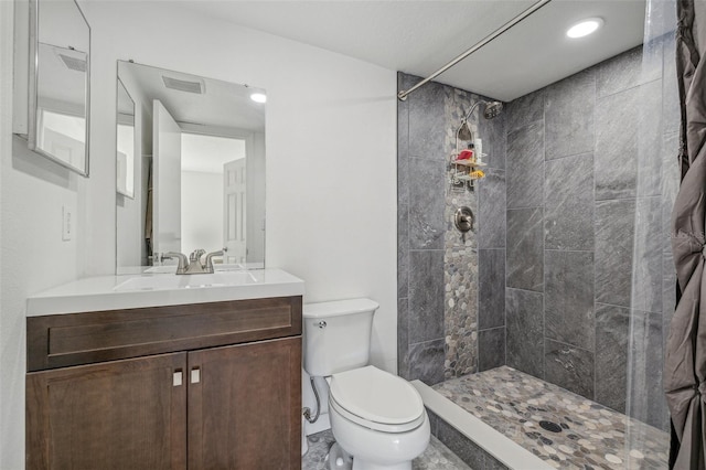 bathroom featuring toilet, tiled shower, and vanity