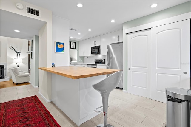 kitchen with a breakfast bar, butcher block countertops, sink, white cabinetry, and stainless steel appliances