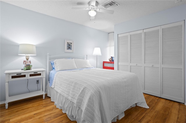 bedroom with a textured ceiling, ceiling fan, a closet, and hardwood / wood-style floors