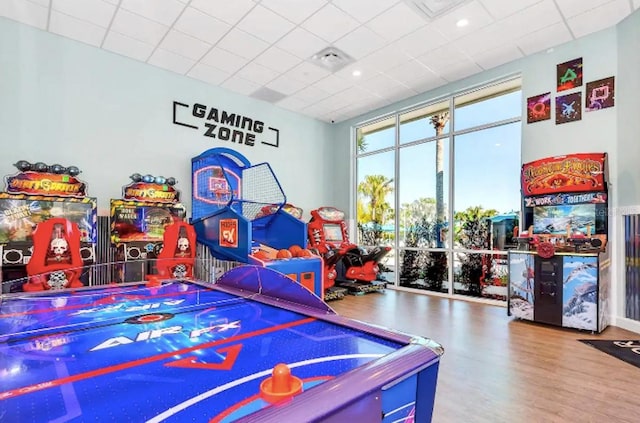 game room with expansive windows, wood-type flooring, and a drop ceiling