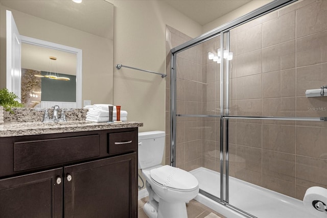 bathroom featuring a shower with shower door, vanity, tile patterned flooring, and toilet