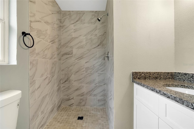 bathroom with vanity, toilet, and tiled shower