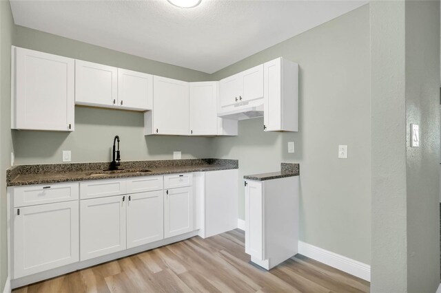 kitchen featuring white cabinetry, sink, dark stone counters, and light wood-type flooring