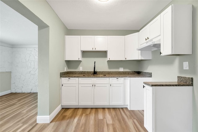 kitchen with sink, dark stone countertops, white cabinets, and light wood-type flooring