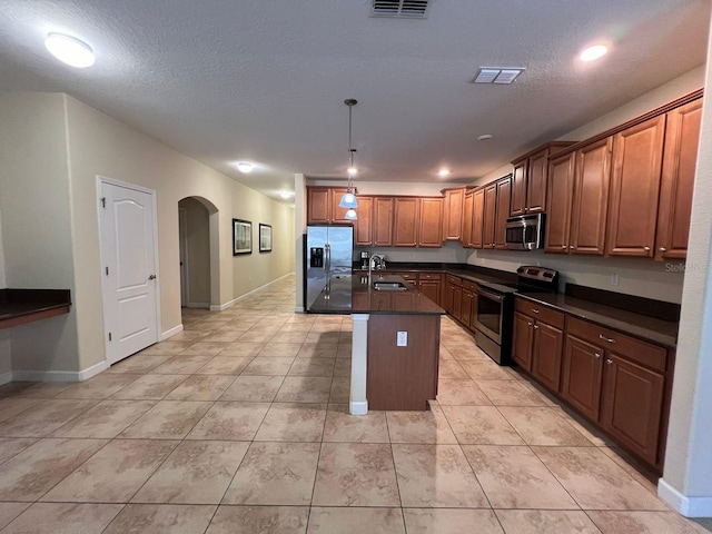 kitchen with a center island with sink, appliances with stainless steel finishes, hanging light fixtures, a textured ceiling, and sink